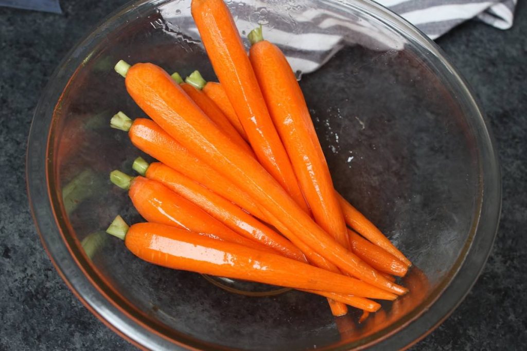 Les carottes épluchées sont assaisonnées de miel et de sel dans un bol transparent.