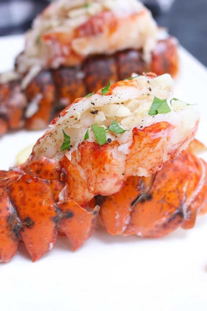 Queues de homard sous vide, saupoudrées de persil haché et servies sur une assiette blanche.