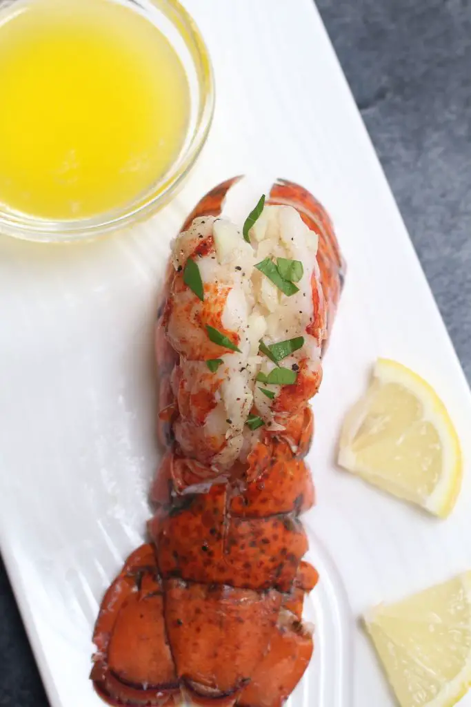 Queues de homard emballées sous vide, servies avec du beurre fondu sur une assiette blanche.