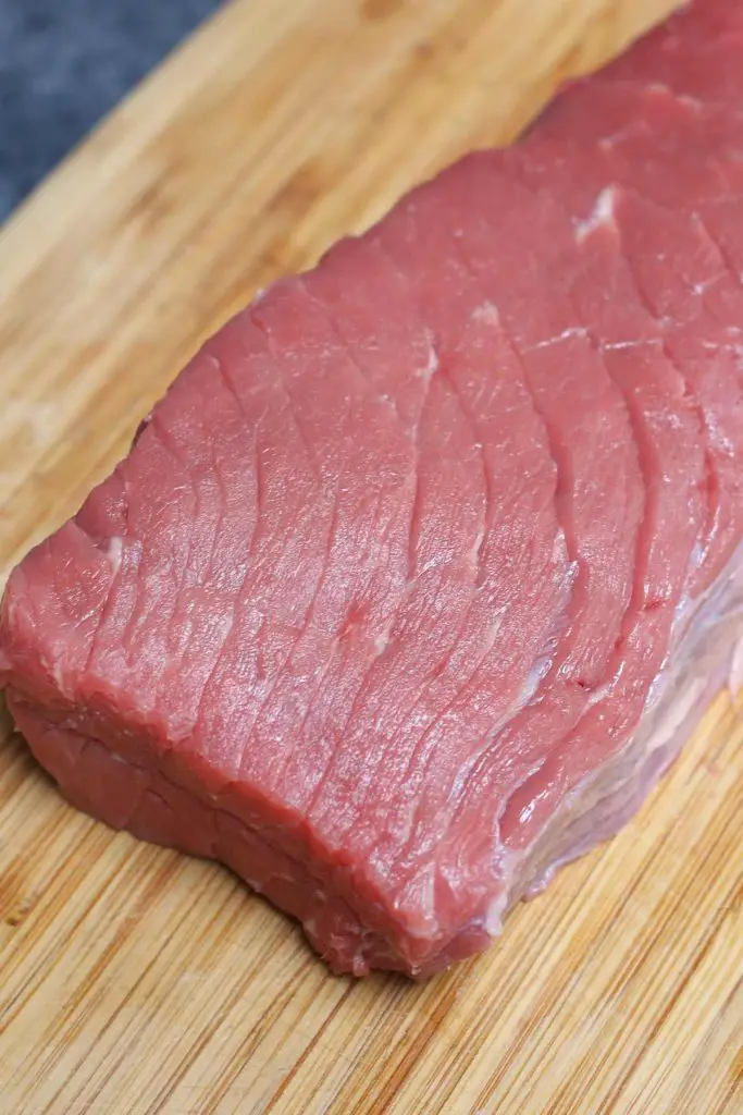 Steak de haut de ronde cru sur une planche à découper.