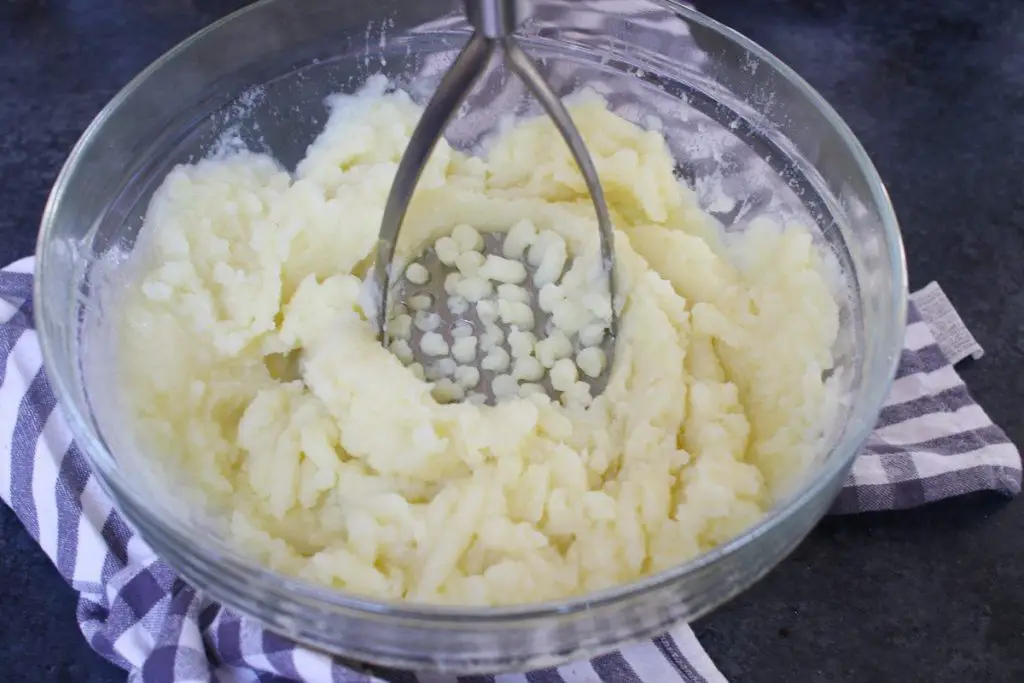 Écraser les pommes de terre cuites à l'aide d'un presse-purée.
